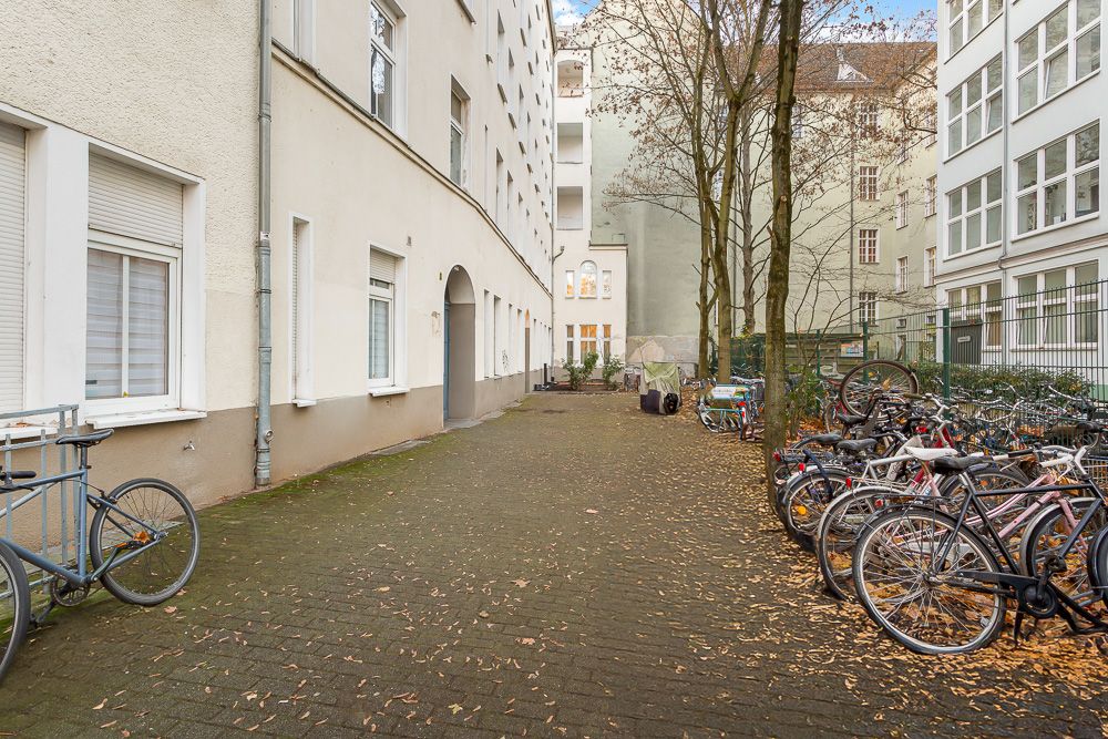 Innenhof mit Pflastersteinen, Bäumen und vielen geparkten Fahrrädern neben Wohnhäusern.