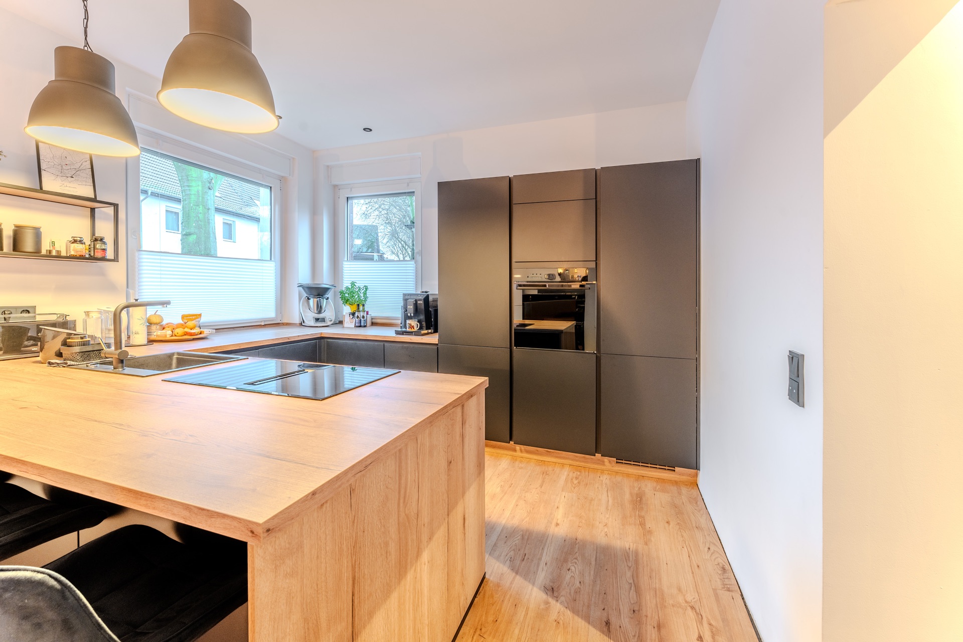 Helle, moderne Küche mit Holzinsel, dunklen Schränken und großen Fenstern.