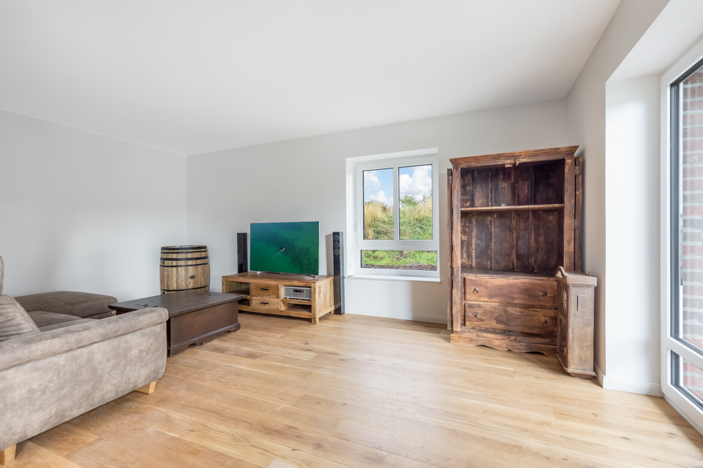 Helles Wohnzimmer mit Holzfußboden, Sofa, Fernseher, Fenster und rustikalen Holzmöbeln.