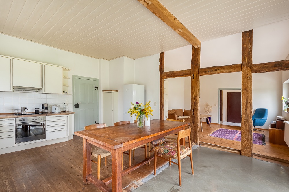 Helle Wohnküche mit Holztisch, Stühlen, Küchenzeile und Blick ins Wohnzimmer.