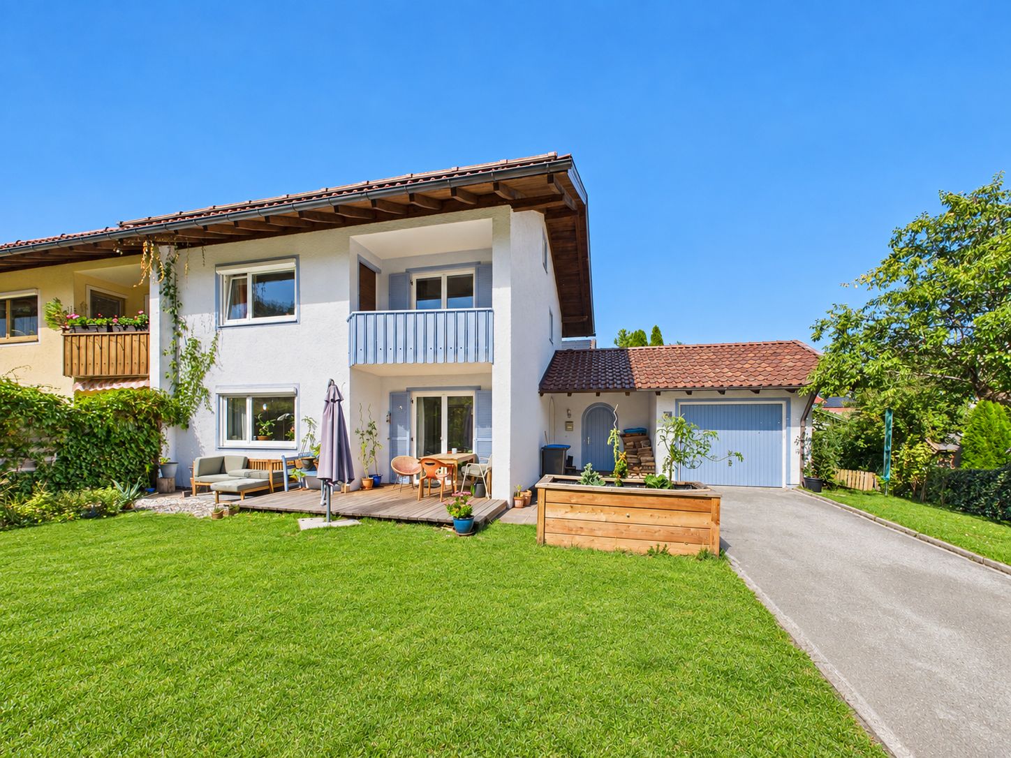 Doppelhaushälfte mit Balkon, Terrasse, Garten und Einfahrt zu einer Garage bei sonnigem Wetter.