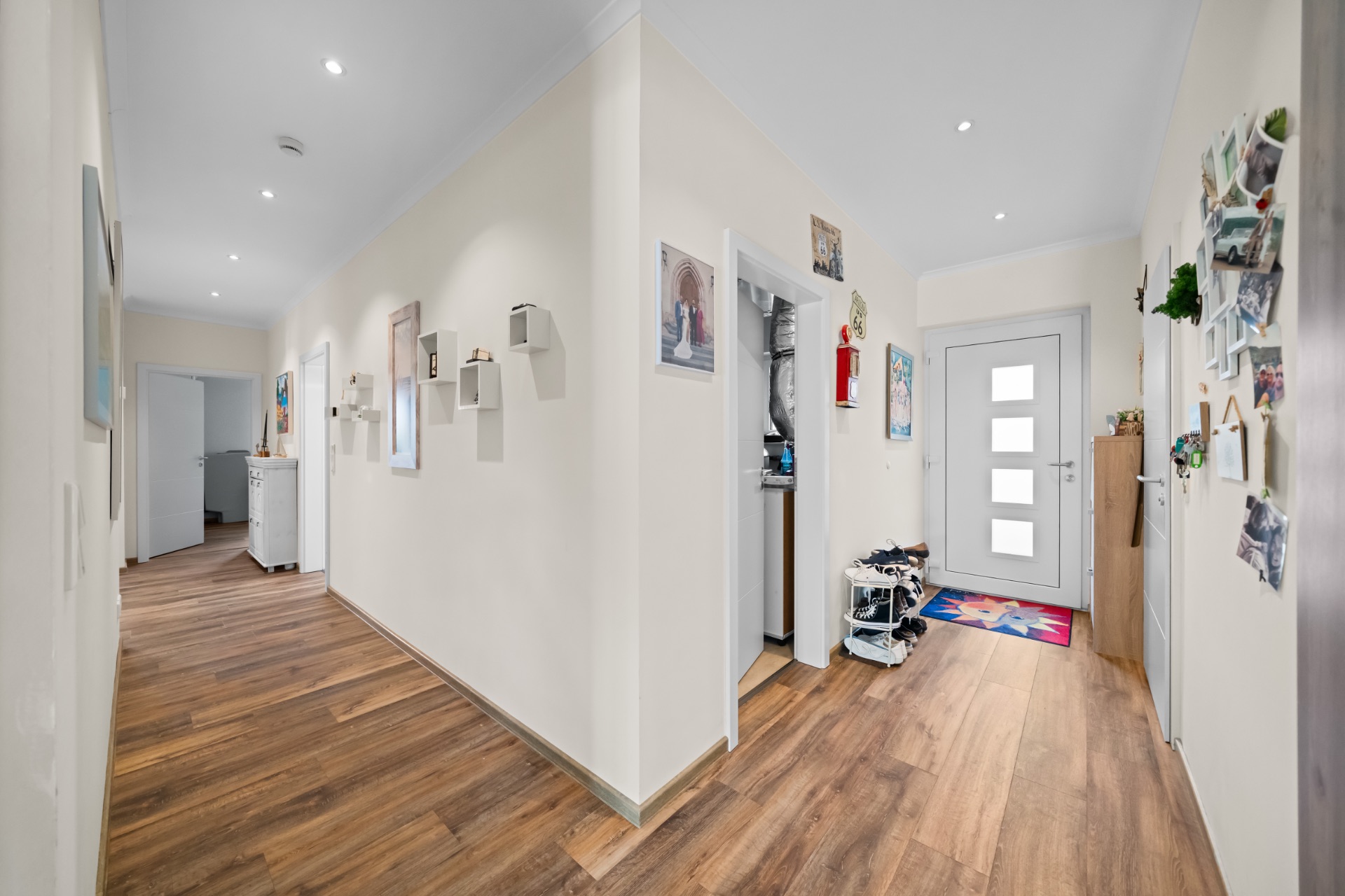 Heller Flur mit Holzboden, mehreren Türen, Wanddekoration und modernen Leuchten.