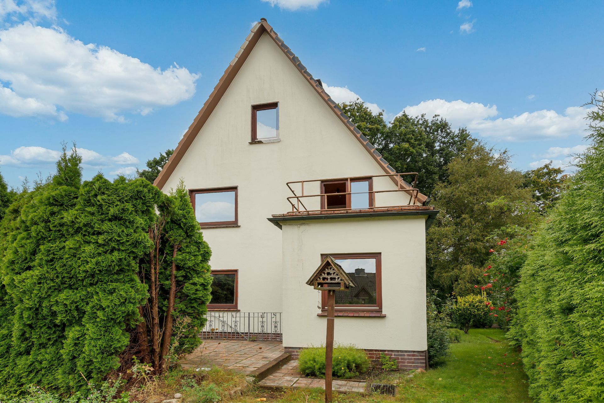 Zweistöckiges Haus mit Satteldach, großem Fenster und Vogelhaus im Garten.