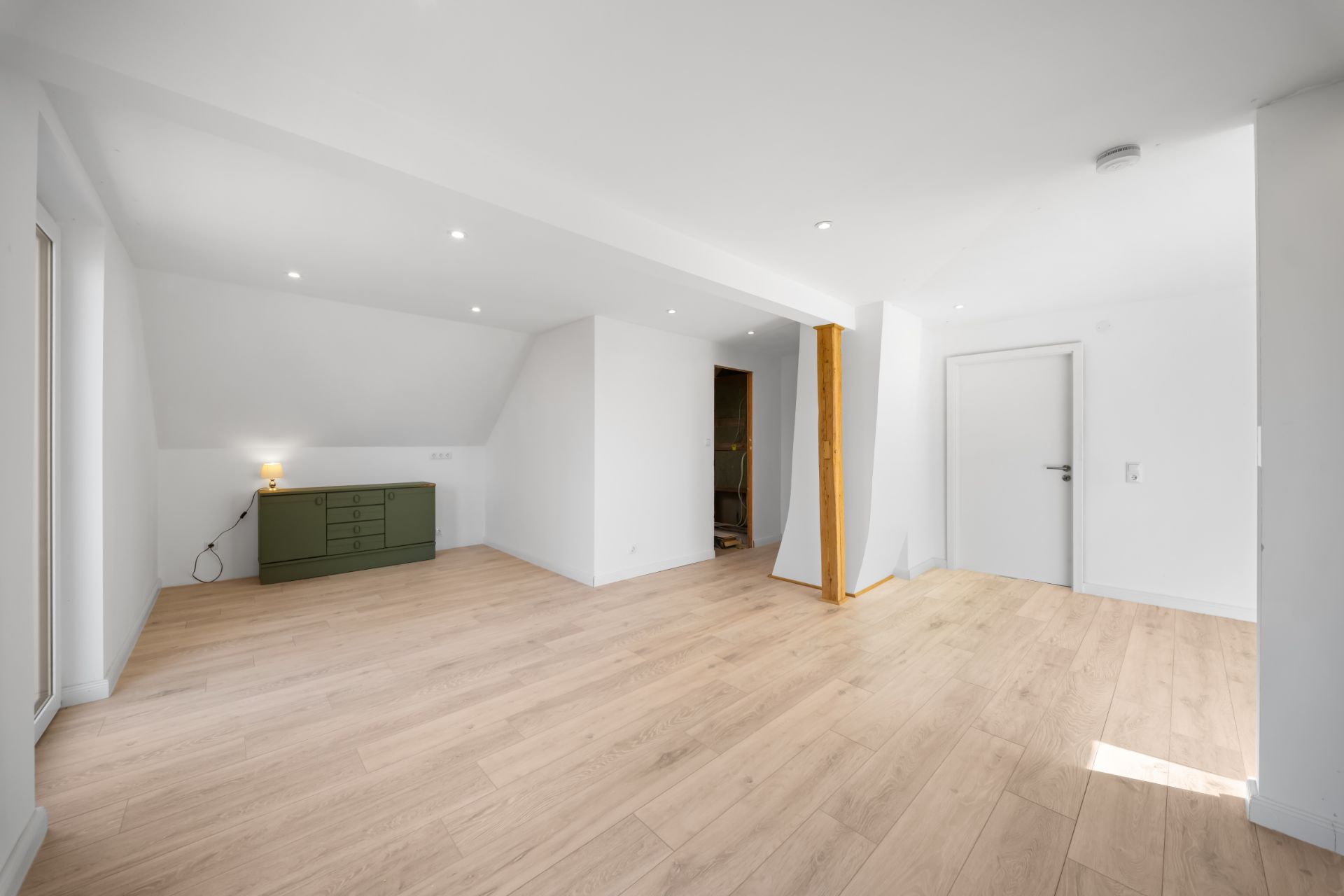 Heller Raum mit Holzfußboden, weiß gestrichenen Wänden und einer grünen Kommode an der Wand.