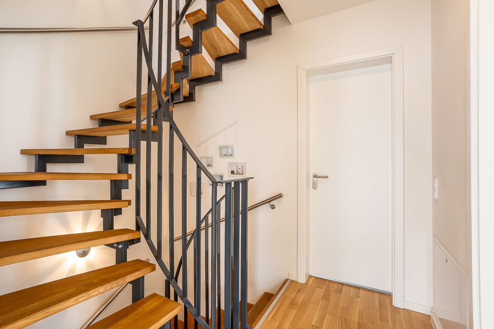 Moderne Holztreppe mit Metallgeländer neben einer weißen Tür in einem Flur.