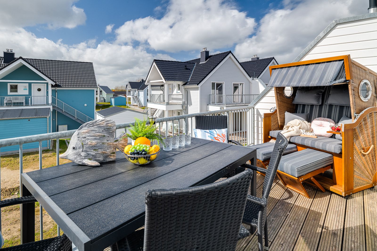 Balkon mit Tisch, Stühlen, Obstschale und Strandkorb, Blick auf Wohnhäuser.