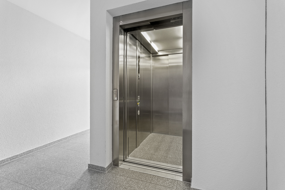 Offener Aufzug mit Edelstahlauskleidung in einem Wohnhausflur.