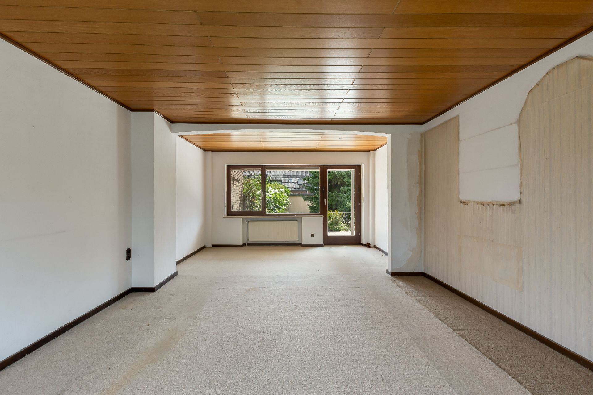 Leerer Raum mit Holzdecke, großem Fenster und Tür zum Garten.