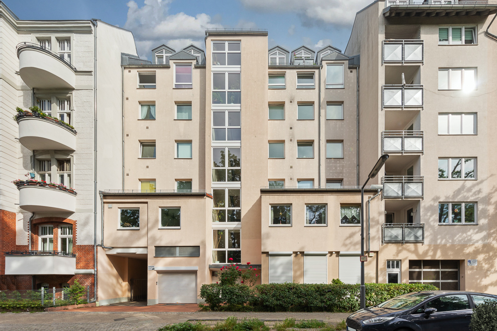 Mehrfamilienhaus mit mehreren Stockwerken und großen Fenstern, umgeben von anderen Wohngebäuden.