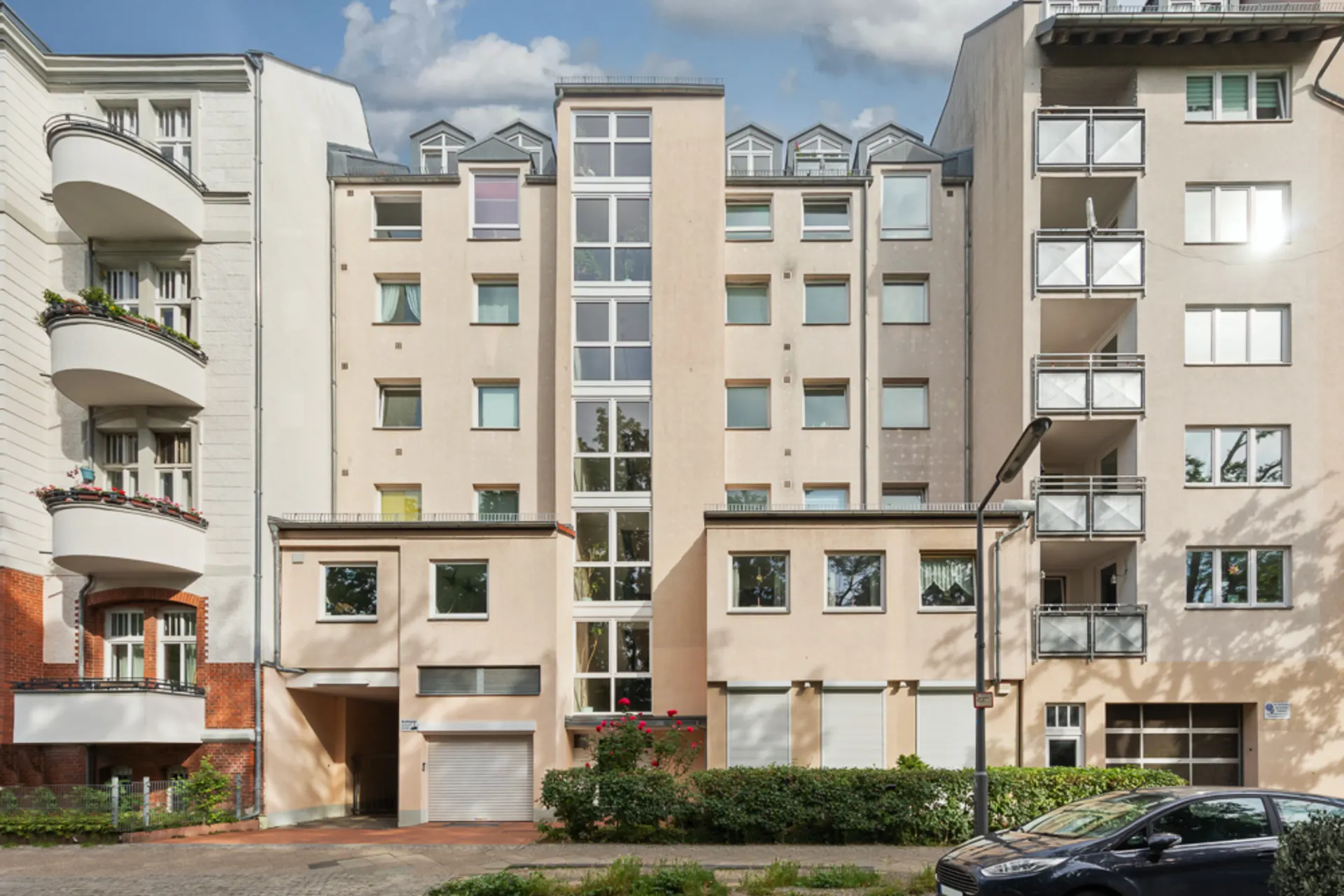 Mehrfamilienhaus mit mehreren Stockwerken und großen Fenstern, umgeben von anderen Wohngebäuden.