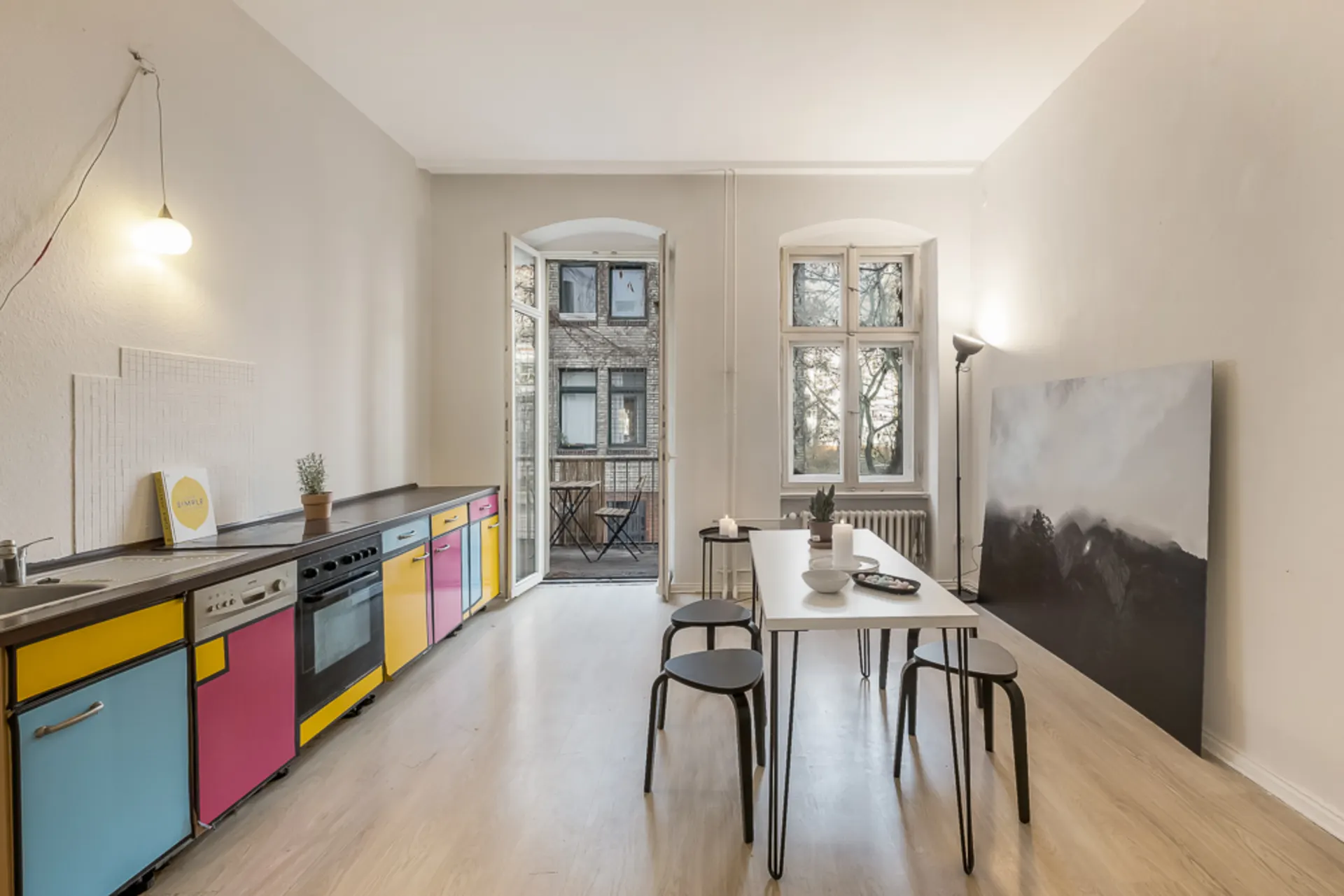 Helle Küche mit bunten Schränken, Esstisch und Zugang zu einem kleinen Balkon.