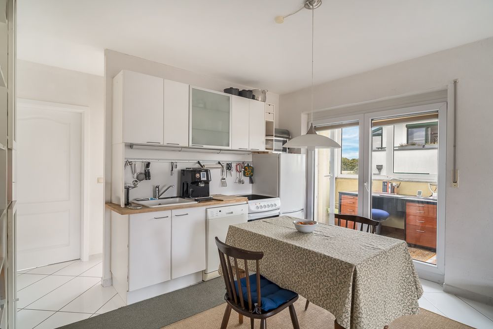 Helle Küche mit Esstisch, Stühlen, weißen Schränken und Zugang zu einem Balkon.