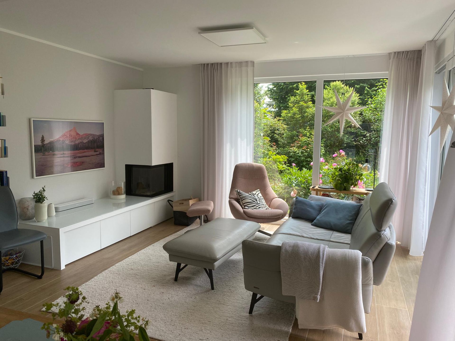 Modernes Wohnzimmer mit Sofa, Sessel, Couchtisch und großen Fenstern mit Blick auf einen Garten.
