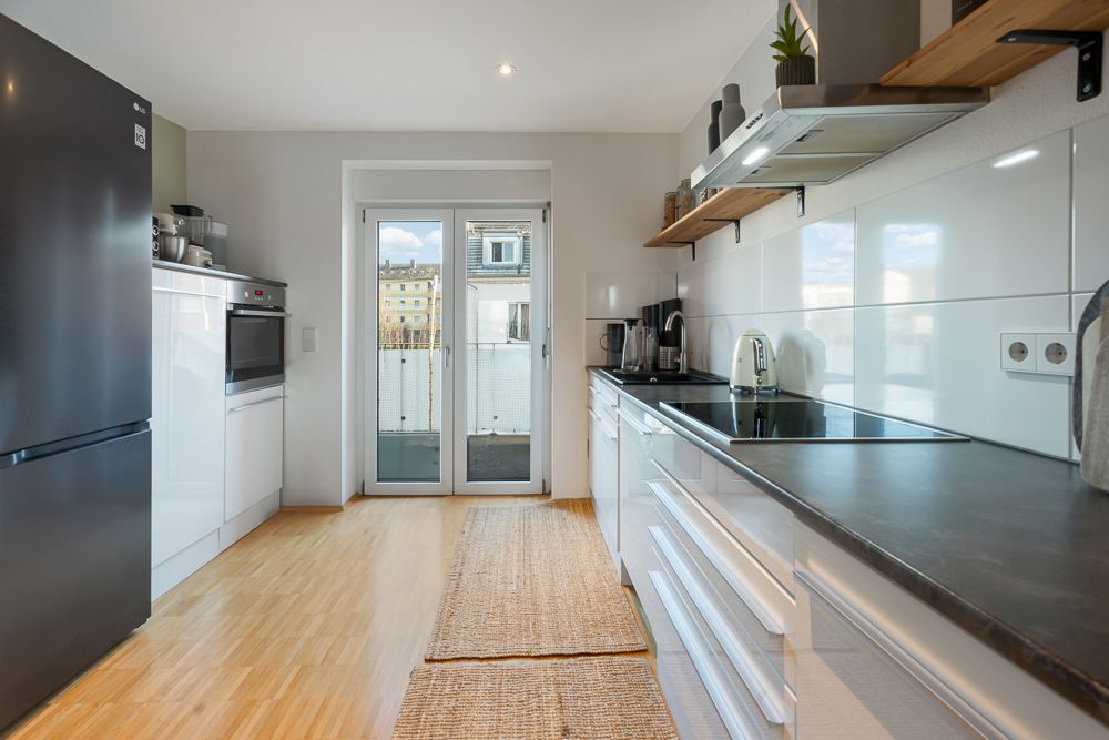 Moderne Küche mit Holzboden, weißen Schränken und Glastür zu einem Balkon.