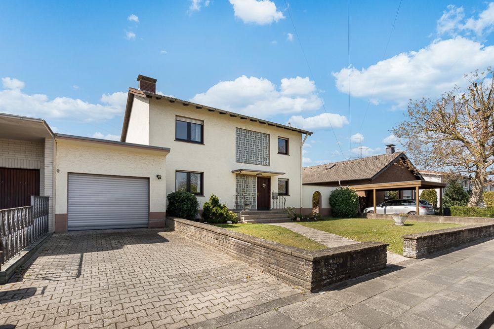 Zweistöckiges Wohnhaus mit Garage, Auffahrt und Vorgarten an einem sonnigen Tag.
