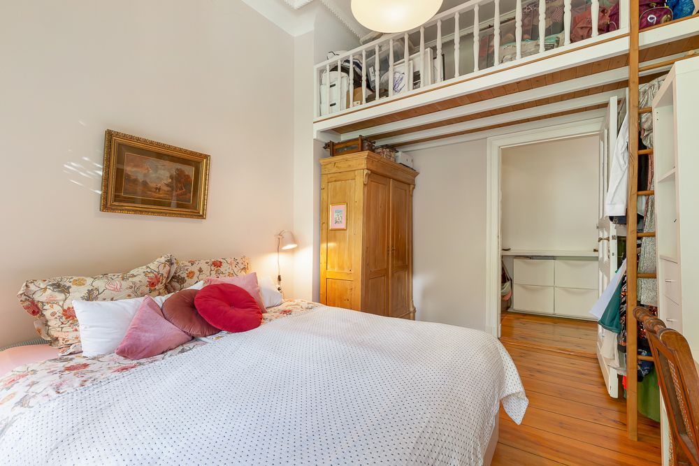 Schlafzimmer mit Doppelbett, Holzschrank und Hochbett mit Geländer und Aufbewahrung.