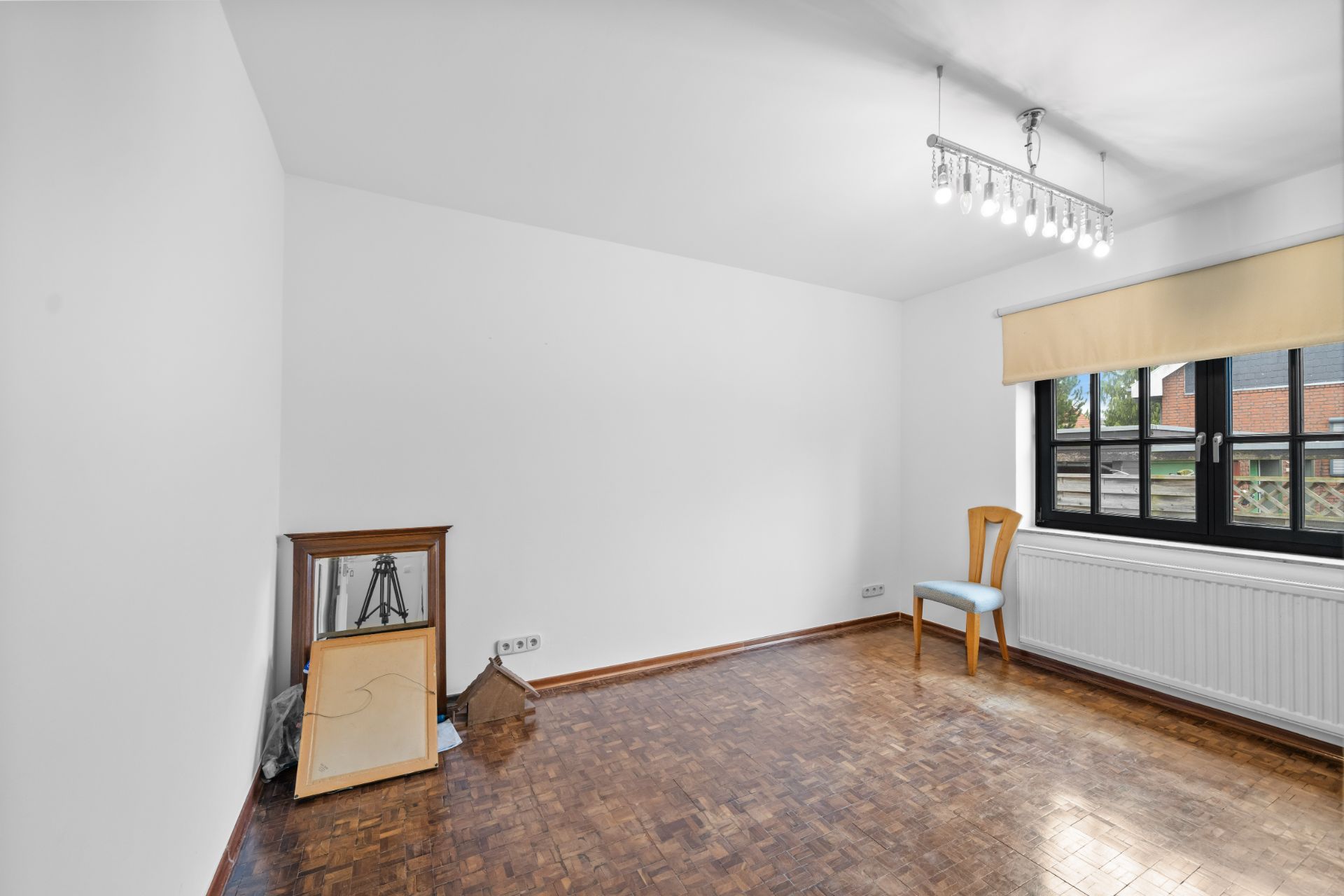 Leeres Zimmer mit Parkettboden, einem Stuhl am Fenster und Glasvitrine in der Ecke.