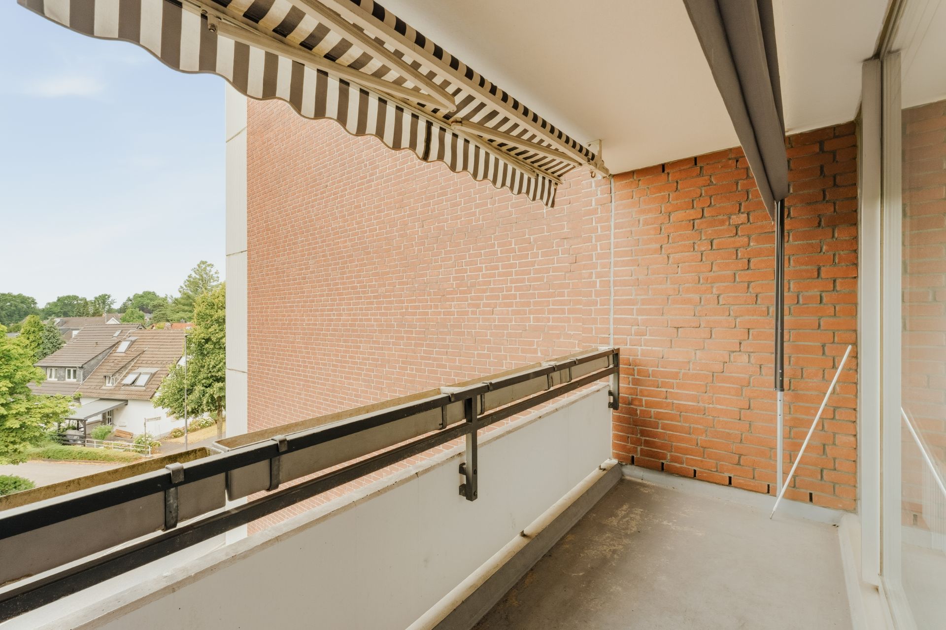 Balkon mit Markise, Backsteinwand und Blick auf Nachbarhäuser und Bäume.