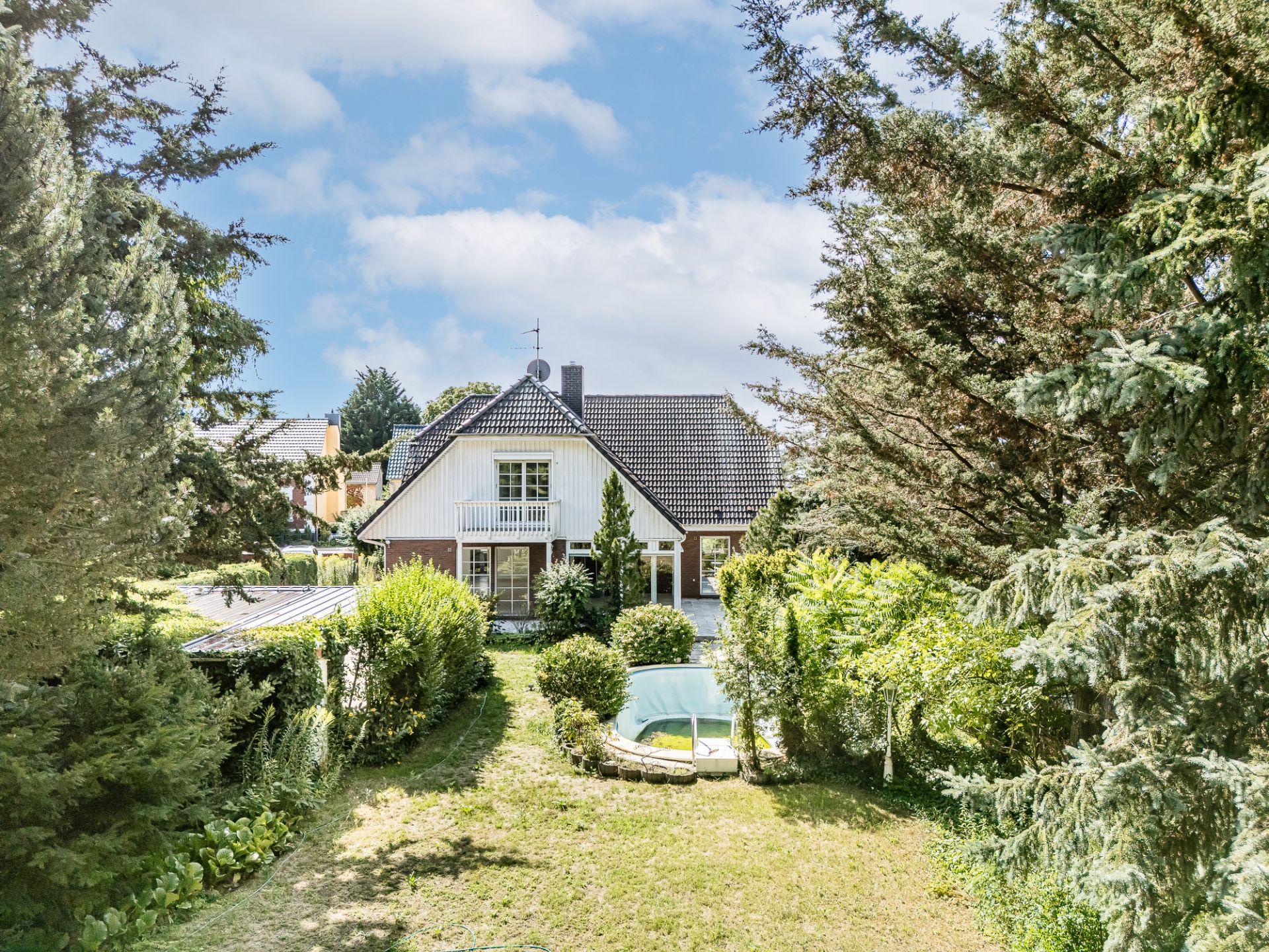 Haus mit Satteldach, großem Garten und kleinem runden Pool, umgeben von Bäumen.