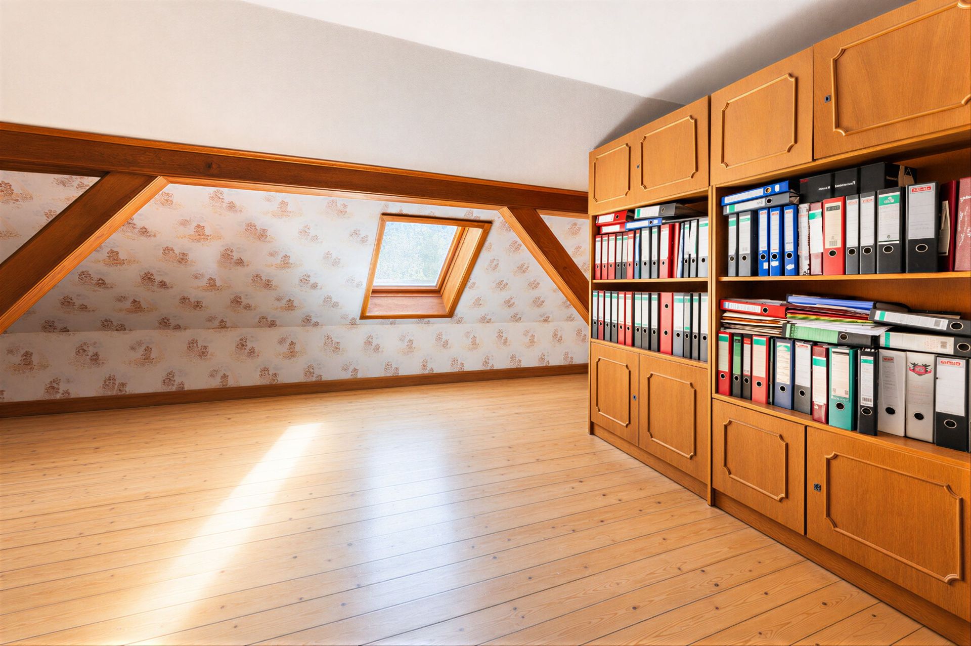 Dachzimmer mit Holzregal voller Aktenordner, schräger Decke und Dachfenster.