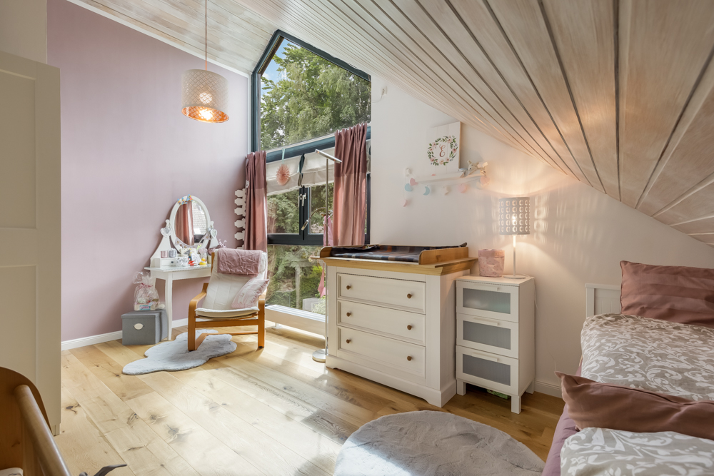Helles Kinderzimmer mit rosa Wand, Möbeln, großem Fenster und Holzdecke.