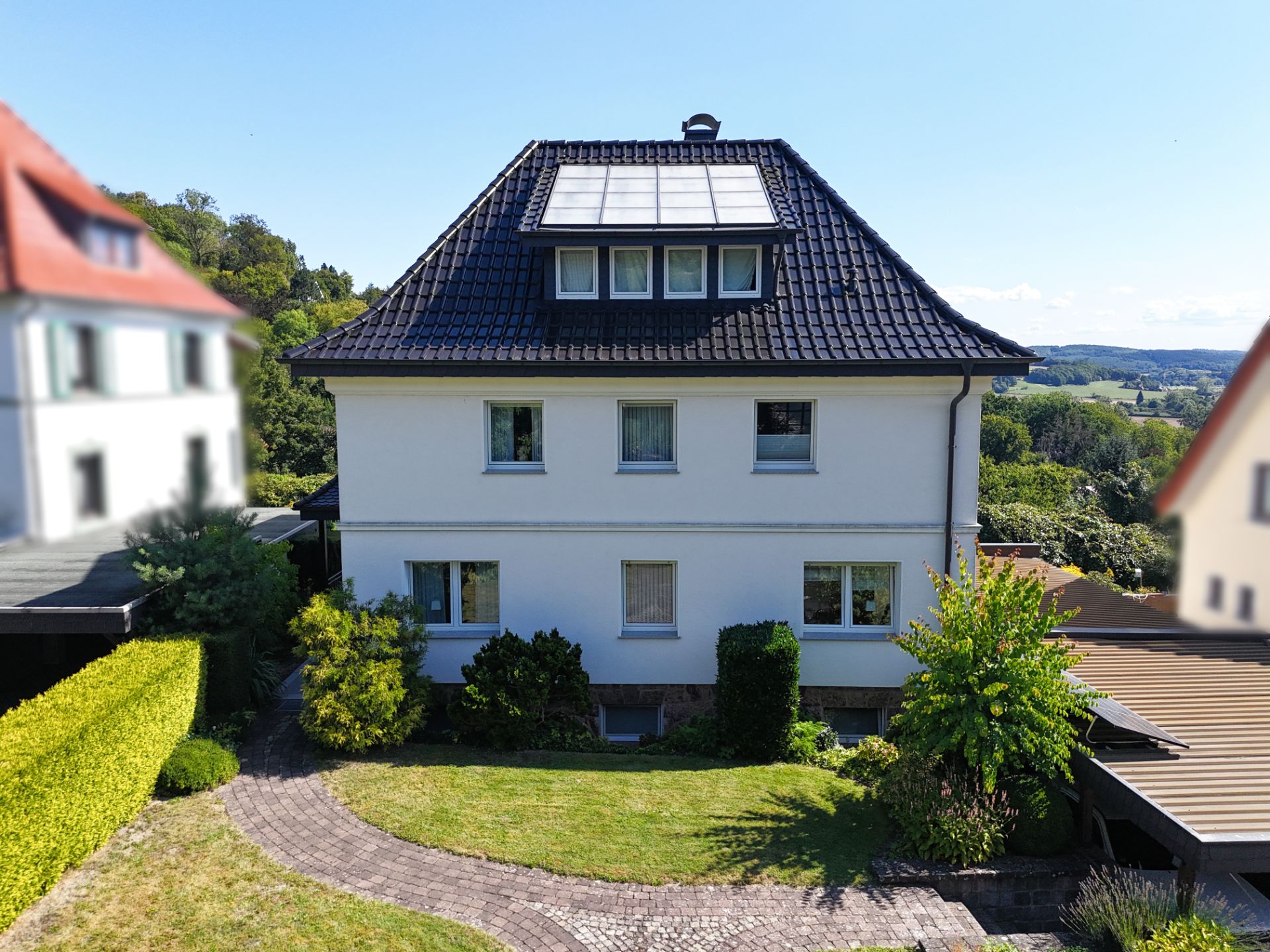 Zweistöckiges Wohnhaus mit dunklem Dach und Solarpanel, gepflegter Garten und Weg im Vordergrund.