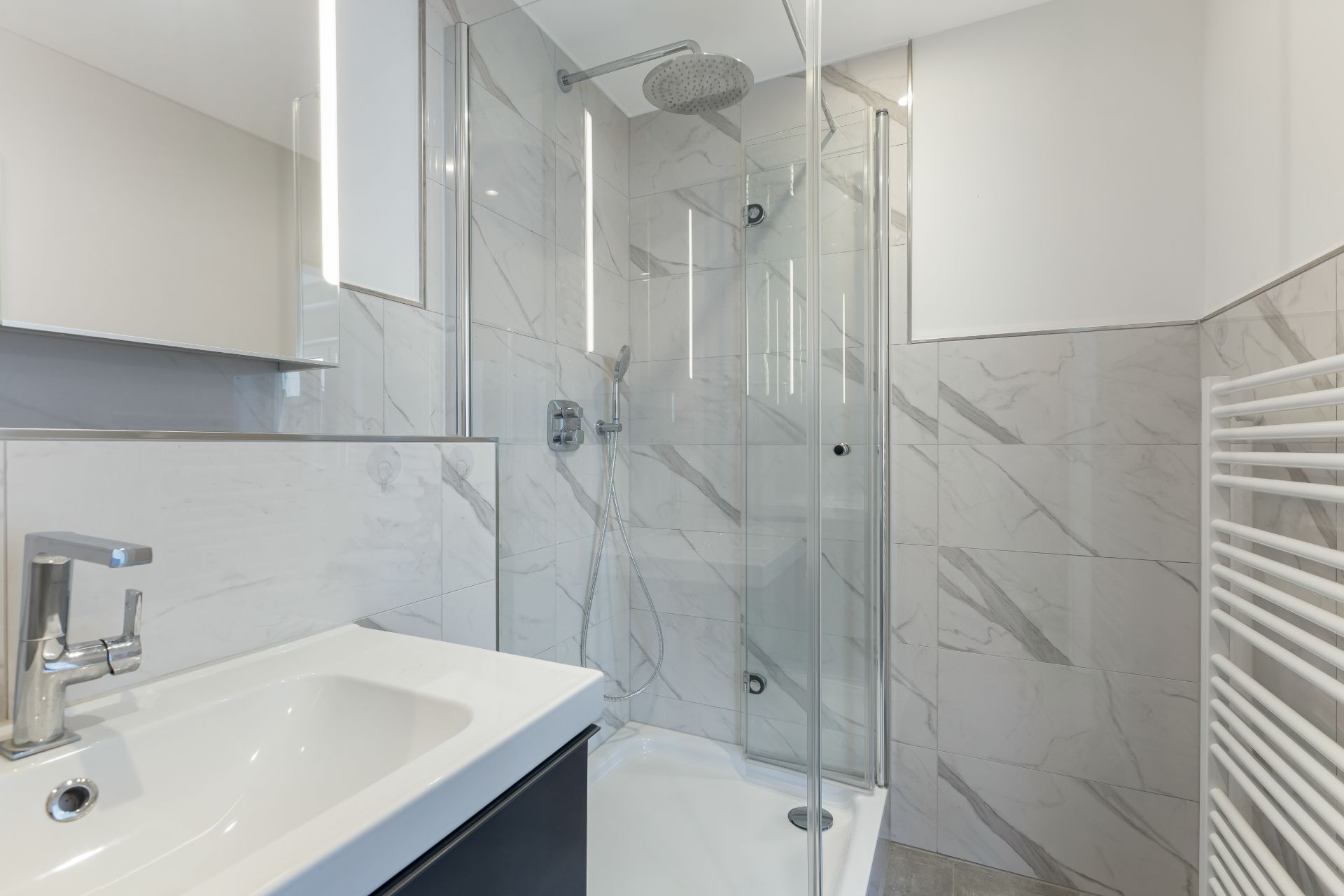Modernes Badezimmer mit Waschbecken, Glasdusche und Handtuchheizkörper.