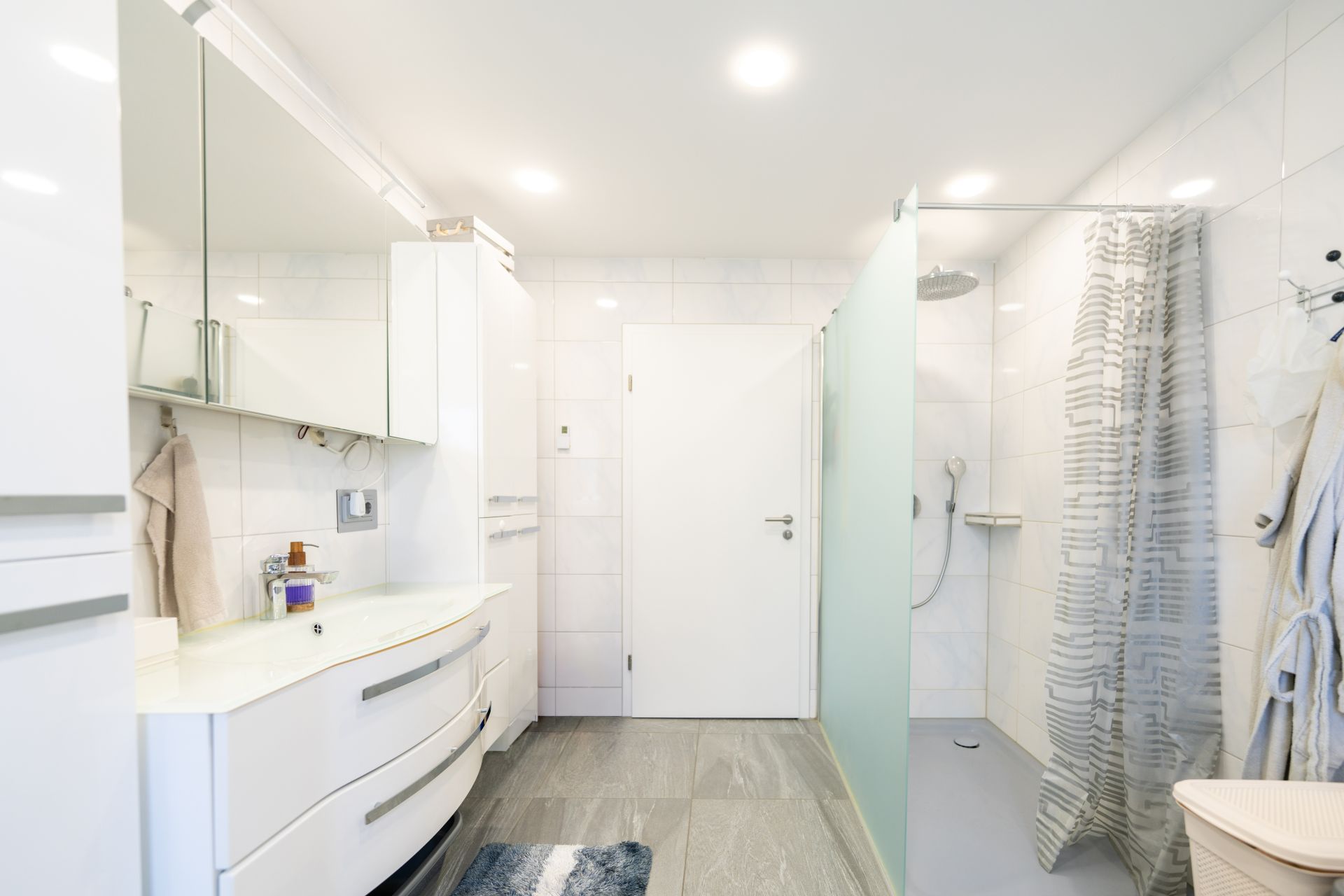 Modernes Badezimmer mit Dusche, Waschbecken, Spiegel und weißen Schränken.