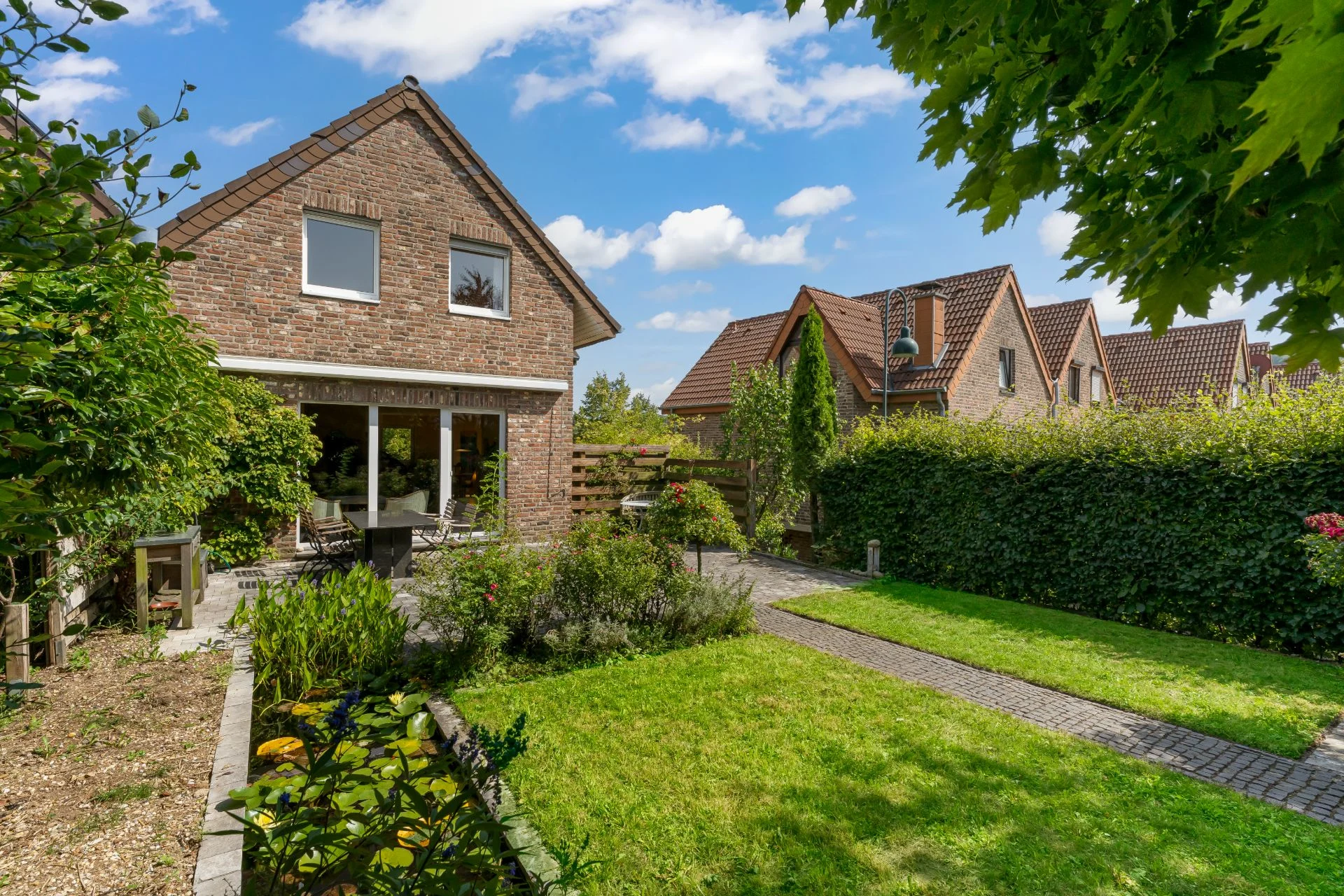 Backsteinwohnhaus mit großem gepflegtem Garten, Rasen und Sträuchern vor dem Haus.