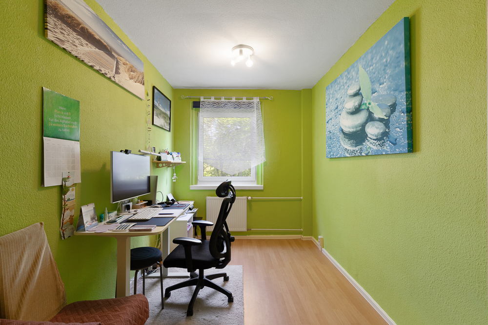Kleines Arbeitszimmer mit grün gestrichenen Wänden, Schreibtisch, Stuhl und Fenster.