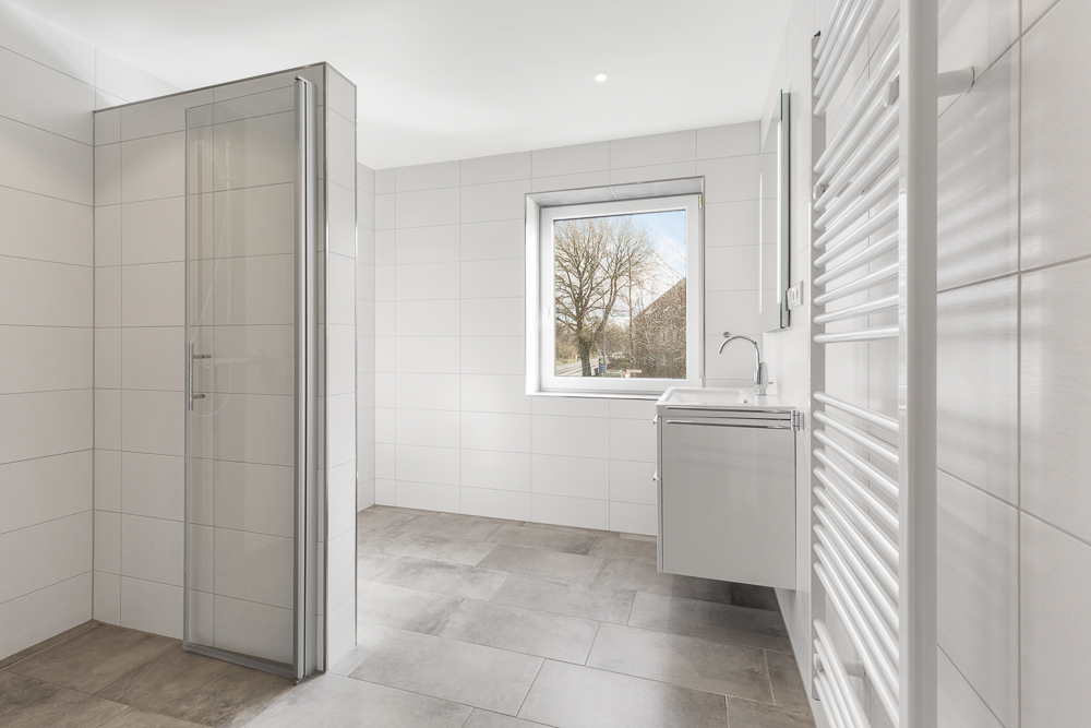 Helles, modernes Badezimmer mit Dusche, Fenster, Waschbecken und Handtuchheizkörper.