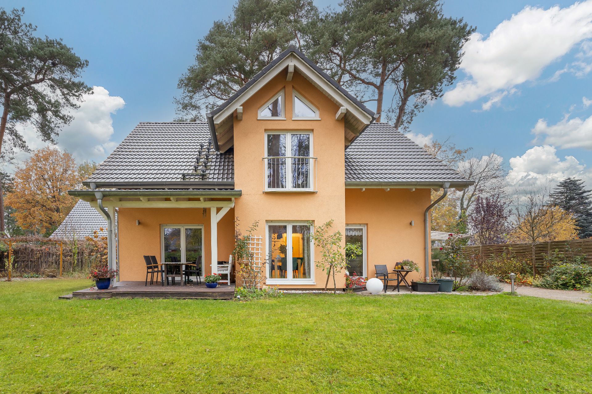 Modernes Einfamilienhaus mit gelber Fassade, Terrasse und Garten, umgeben von Bäumen.