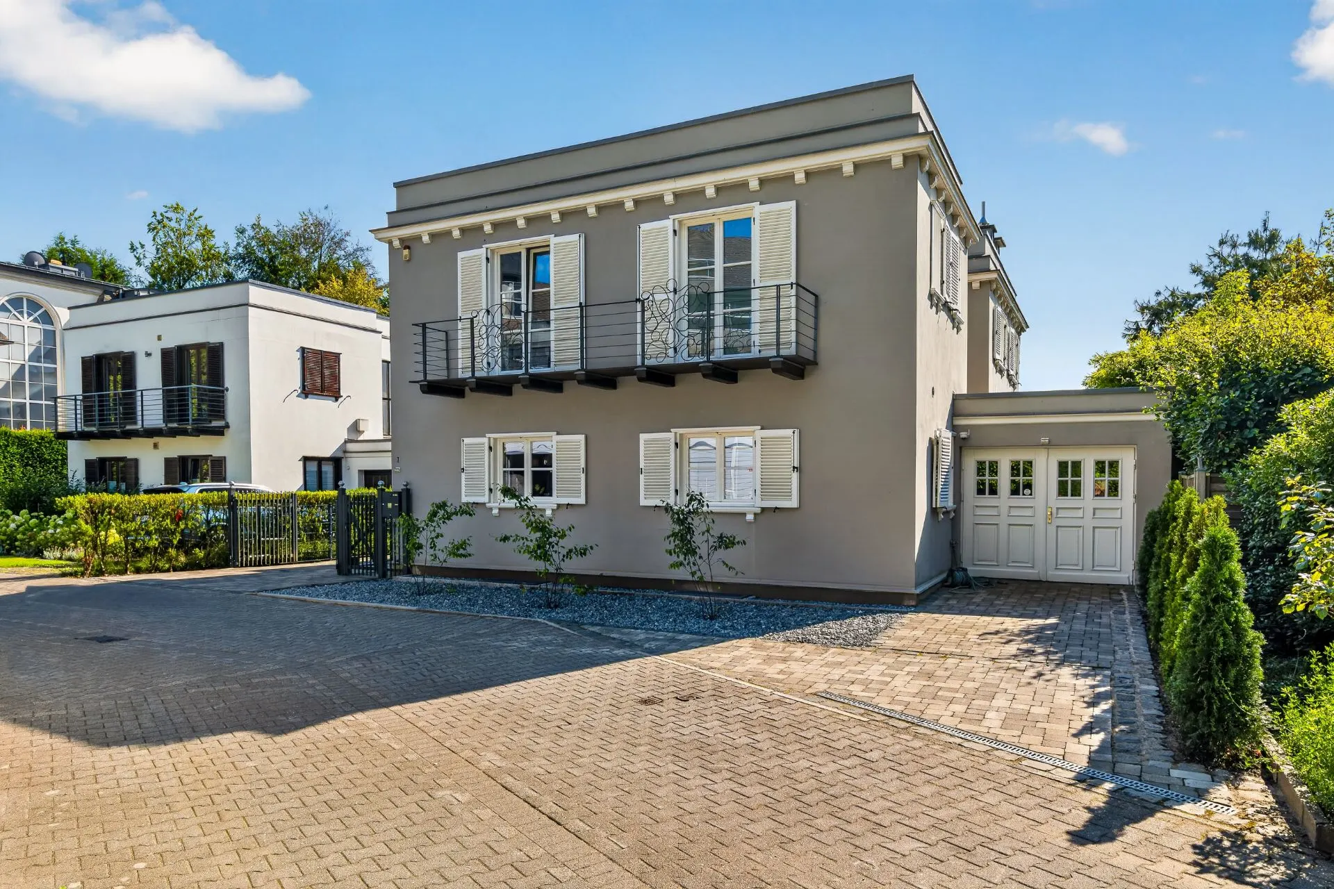 Modernes zweistöckiges Wohnhaus mit weißen Fensterläden, Balkon und gepflasterter Einfahrt.