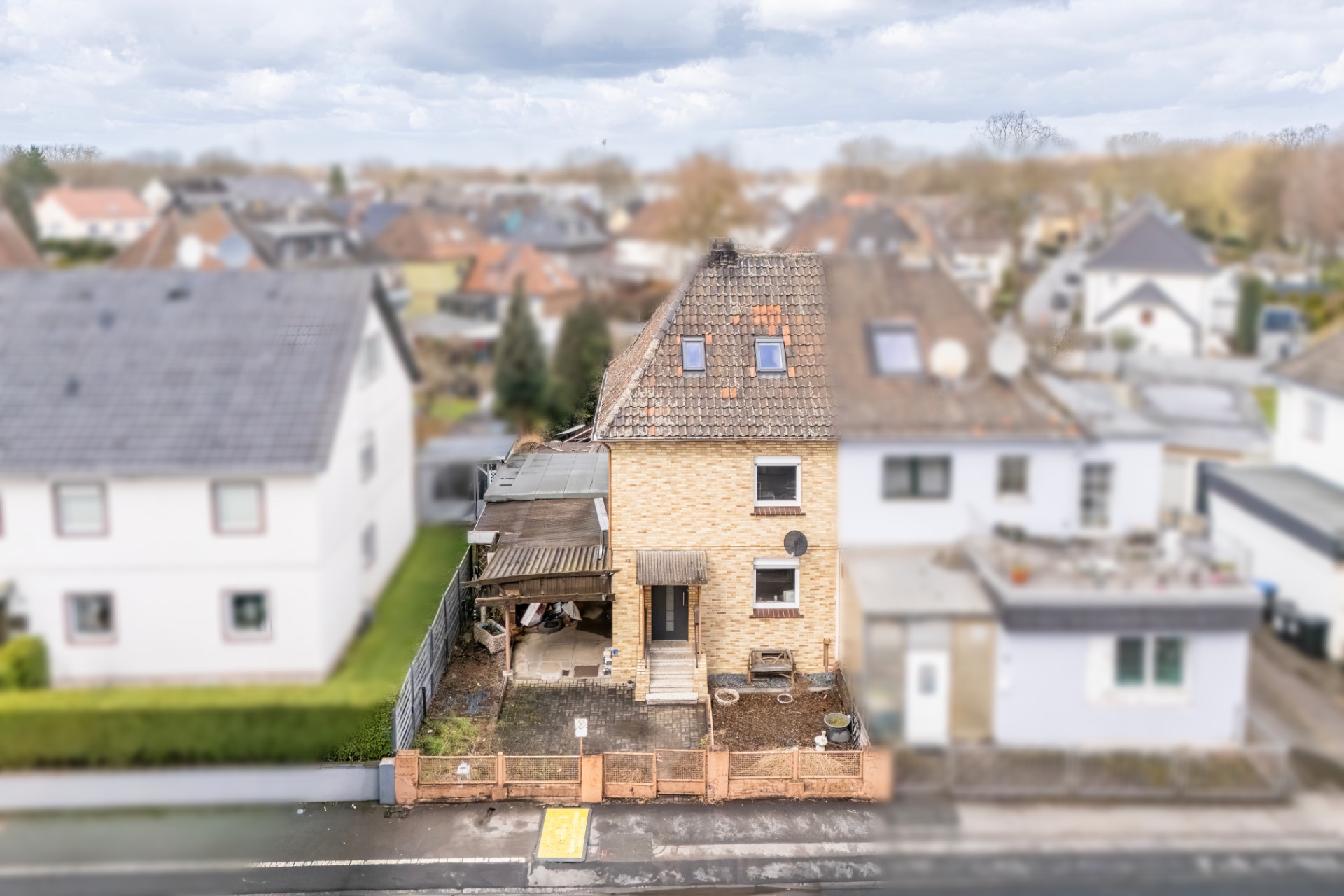 Zweistöckiges Einfamilienhaus mit kleinem Vorgarten und überdachtem Carport an einer Straße.