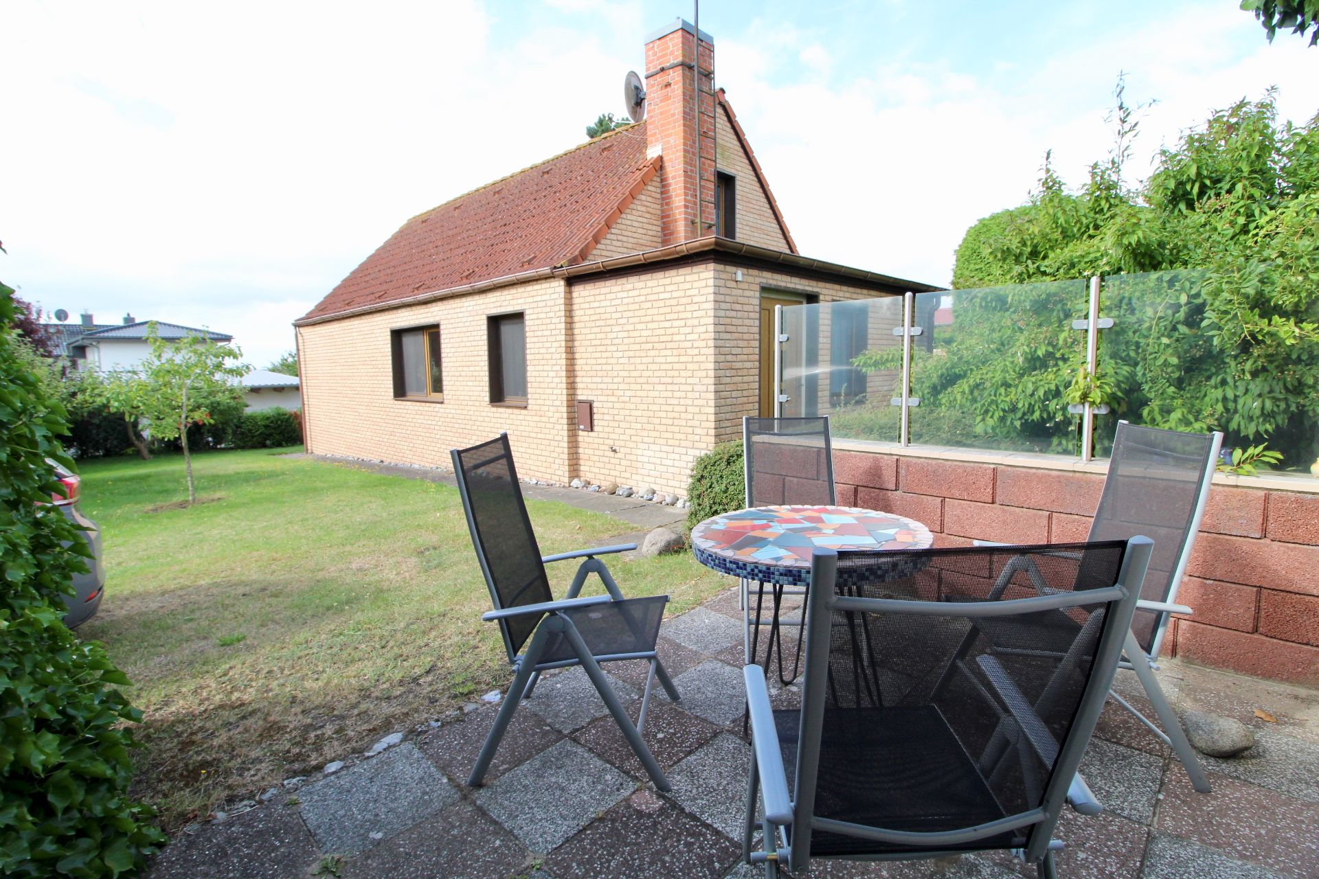 Kleines Haus mit Terrasse, runder Tisch und vier Stühlen im Garten.
