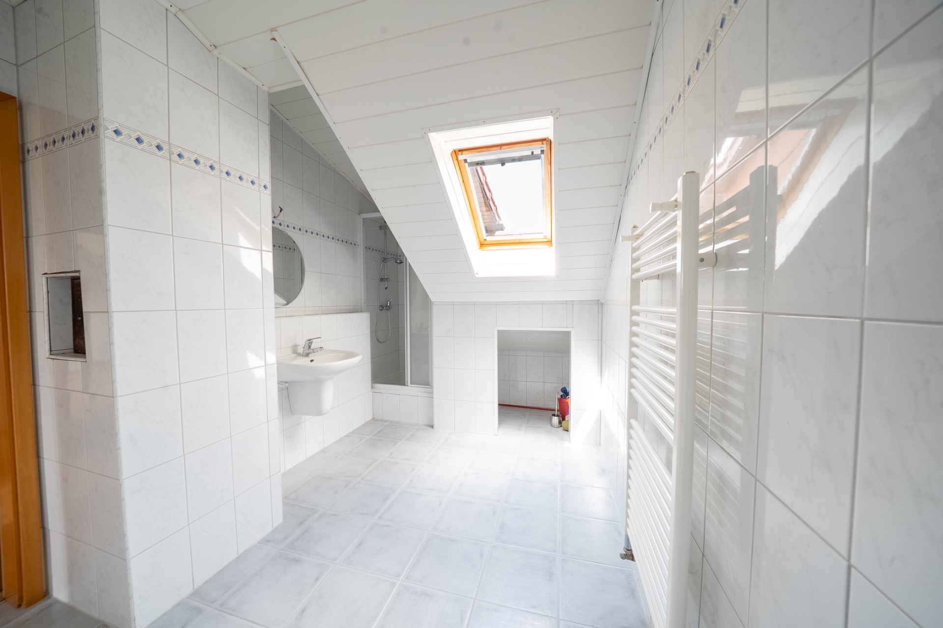 Helles Badezimmer mit Dachfenster, Waschbecken, Dusche und weißen Fliesen.