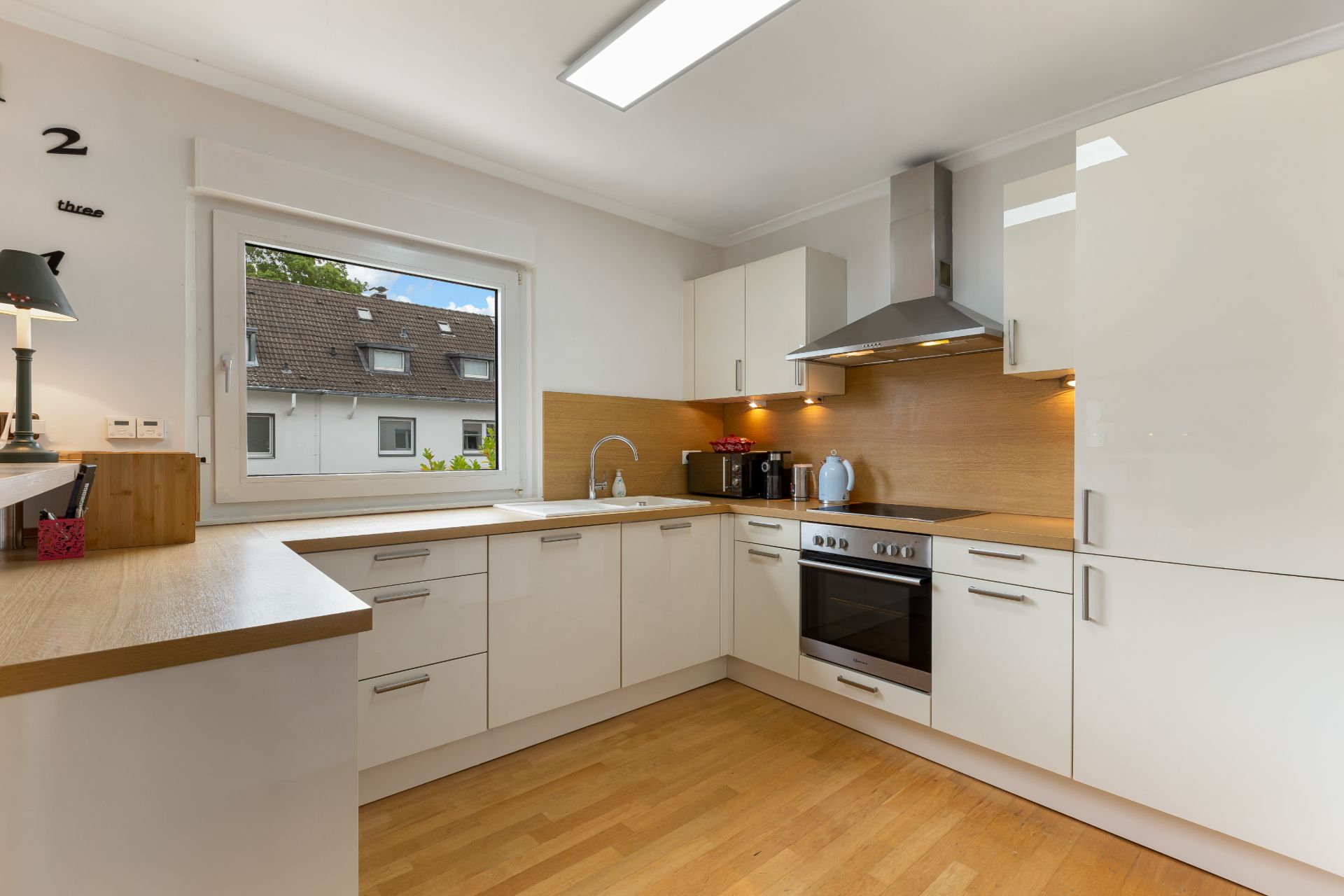 Moderne Küche mit weißen Schränken, Holzarbeitsplatte und großem Fenster.