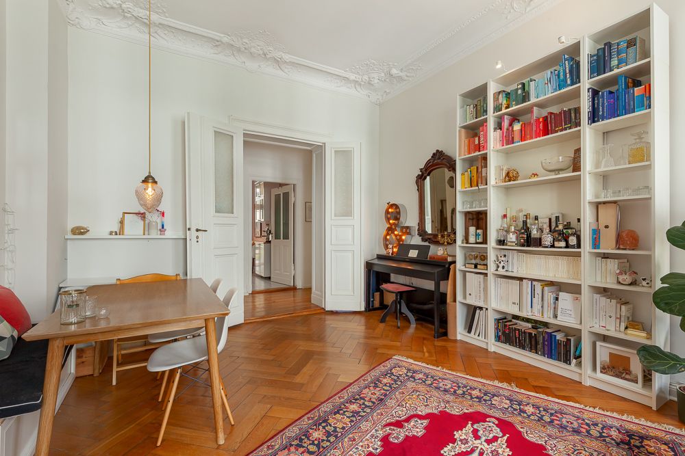 Helles Wohnzimmer mit Esstisch, Bücherregal, Klavier und orientalischem Teppich.