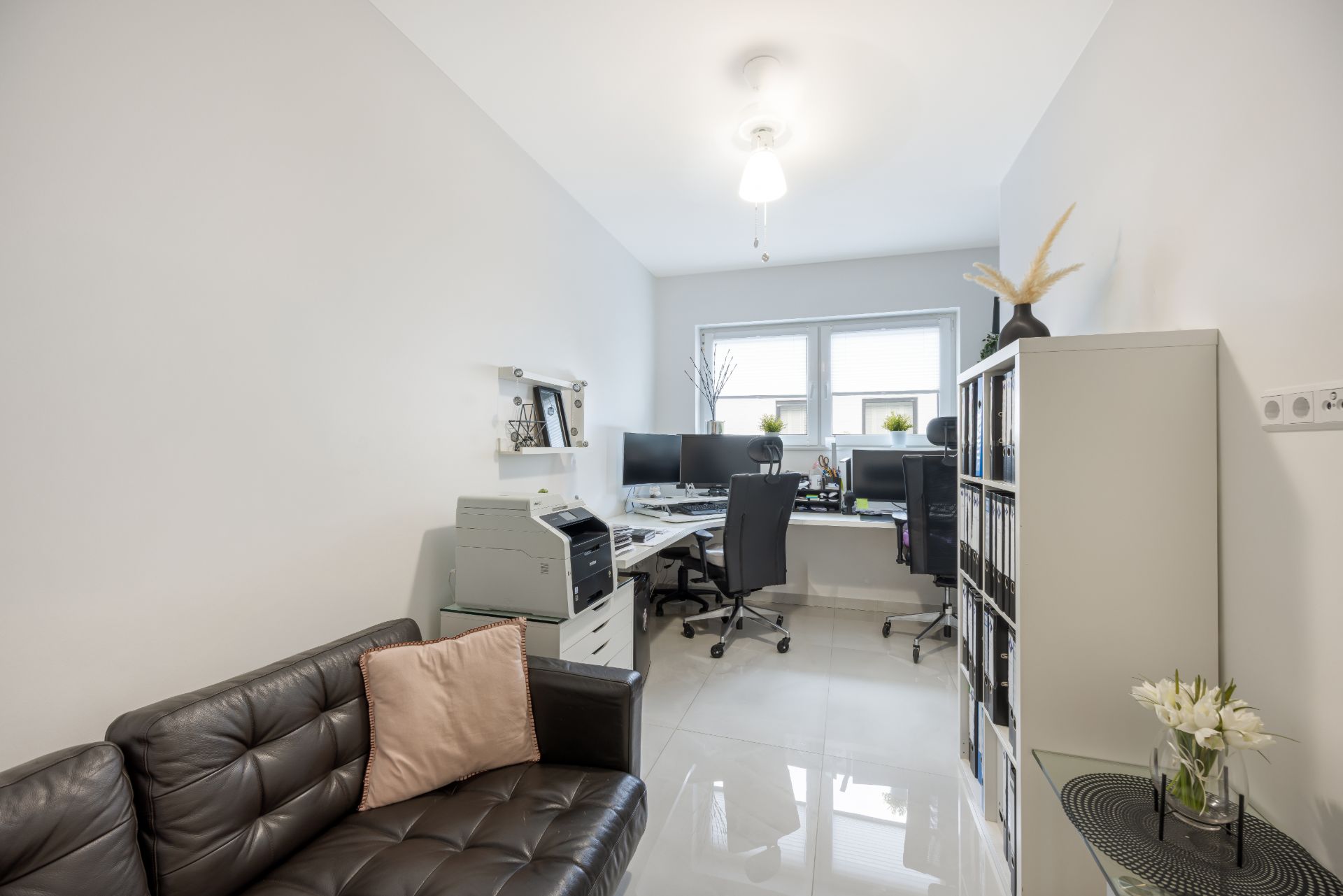 Helles Arbeitszimmer mit Schreibtischen, Bürostühlen, Sofa und Regal, zwei Fenster im Hintergrund.