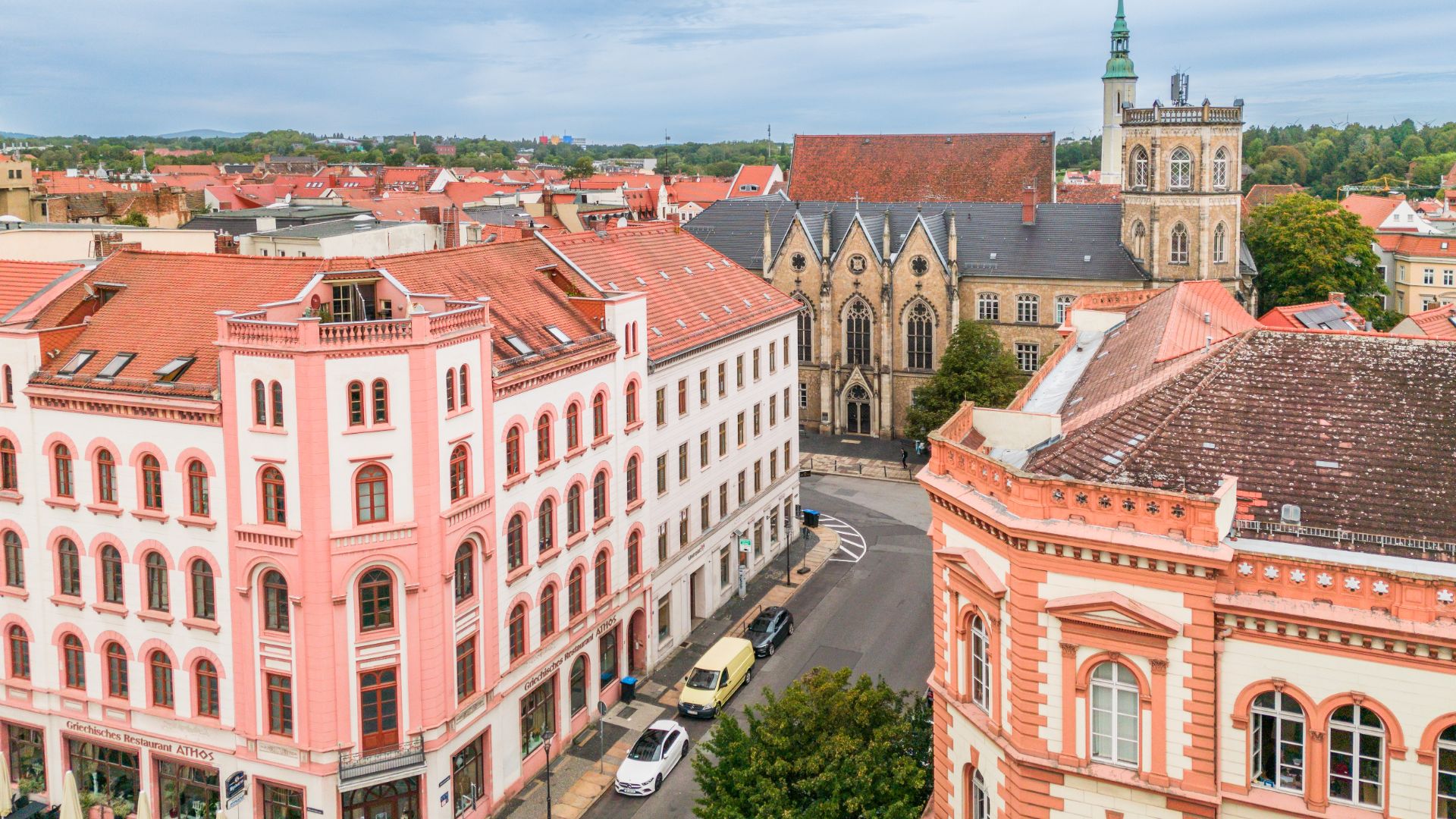 Blick auf mehrere historische Wohngebäude mit roten Dächern und eine Kirche im Hintergrund.