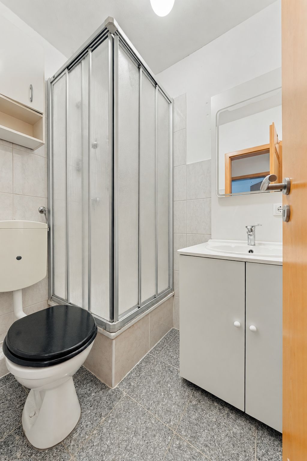 Kleines Bad mit Dusche, WC, Waschbecken und Spiegel.