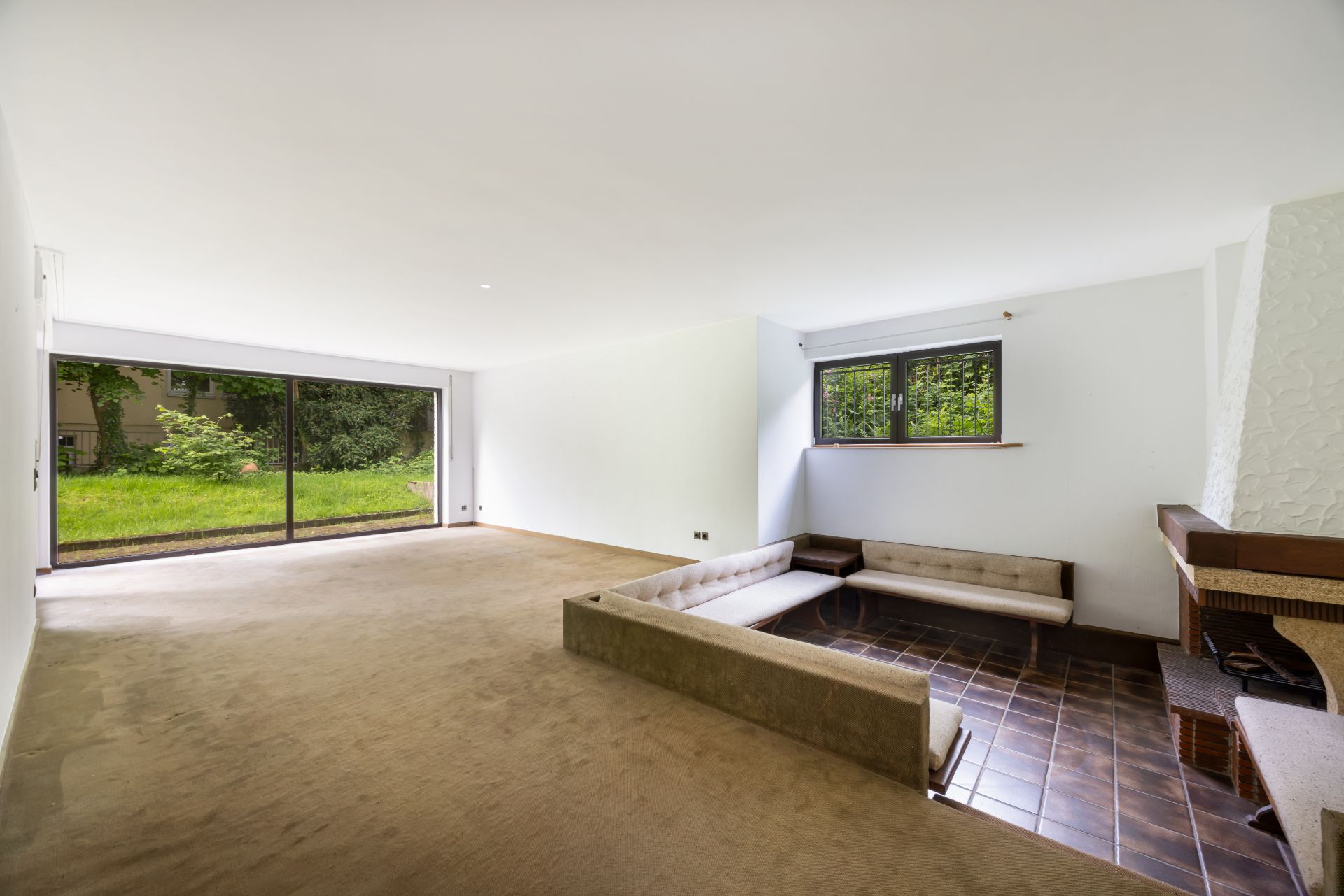 Wohnzimmer mit großem Fenster, versenkter Sitzecke und Blick auf den Garten.
