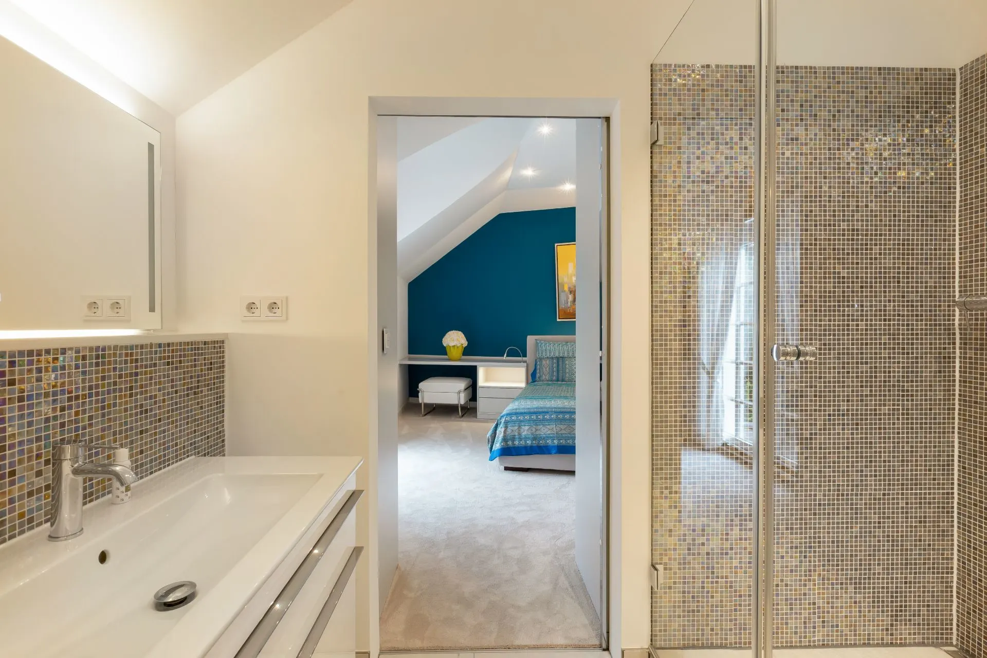 Badezimmer mit Waschbecken und Dusche, Blick ins Schlafzimmer mit blauem Bett.