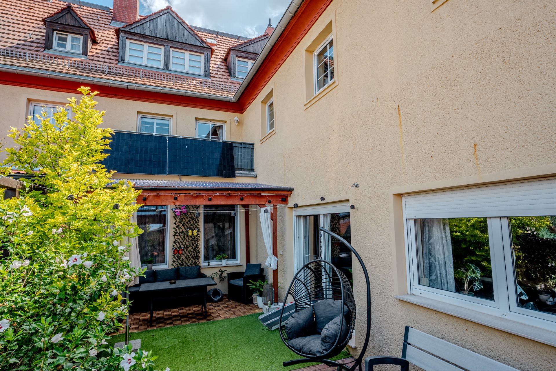 Innenhof mit Terrasse, Gartenmöbeln, Schaukelstuhl und Pflanzen vor einem Mehrfamilienhaus.