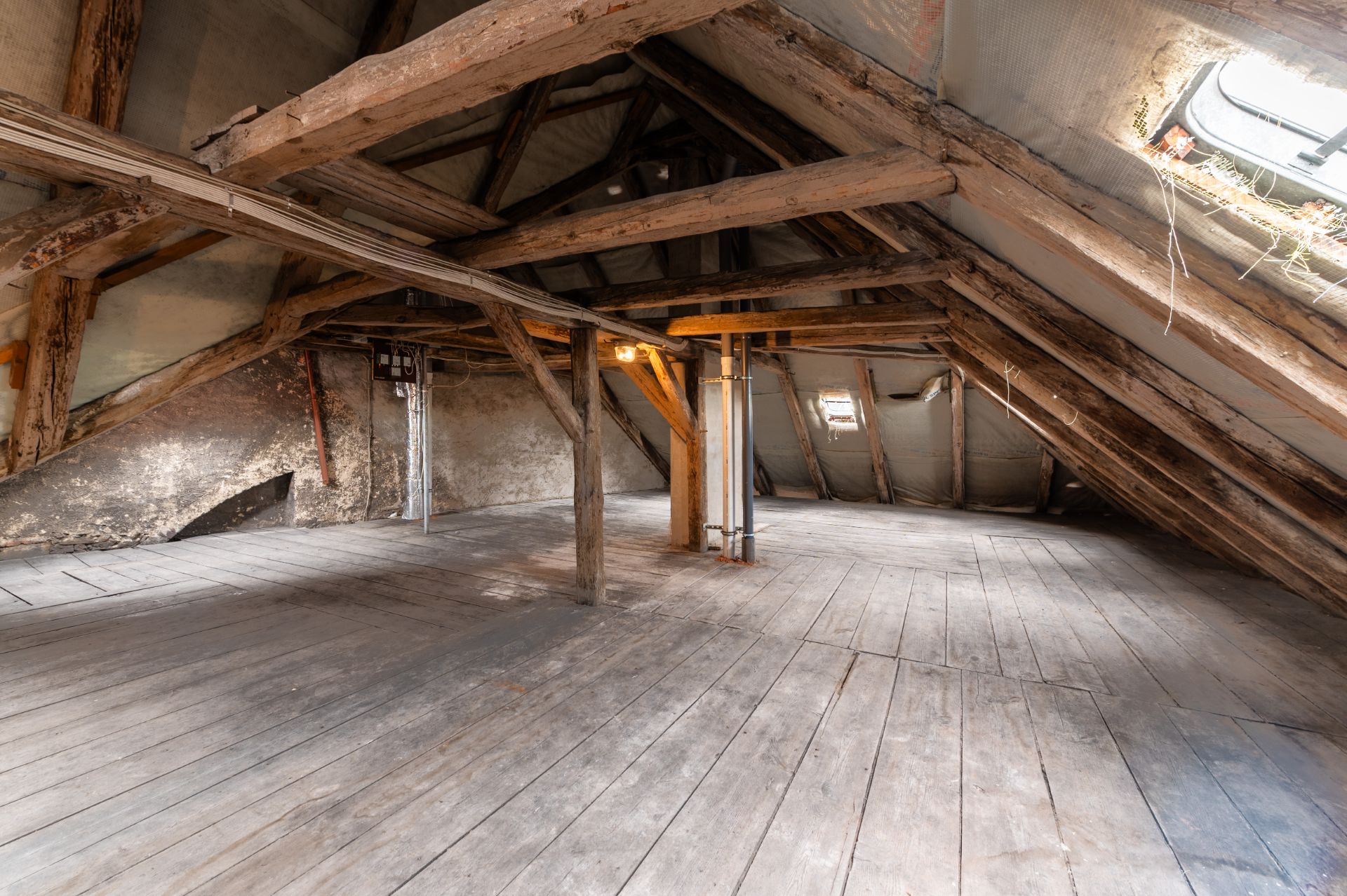 Leerer Dachboden mit Holzbalken, Holzboden und zwei kleinen Dachfenstern.