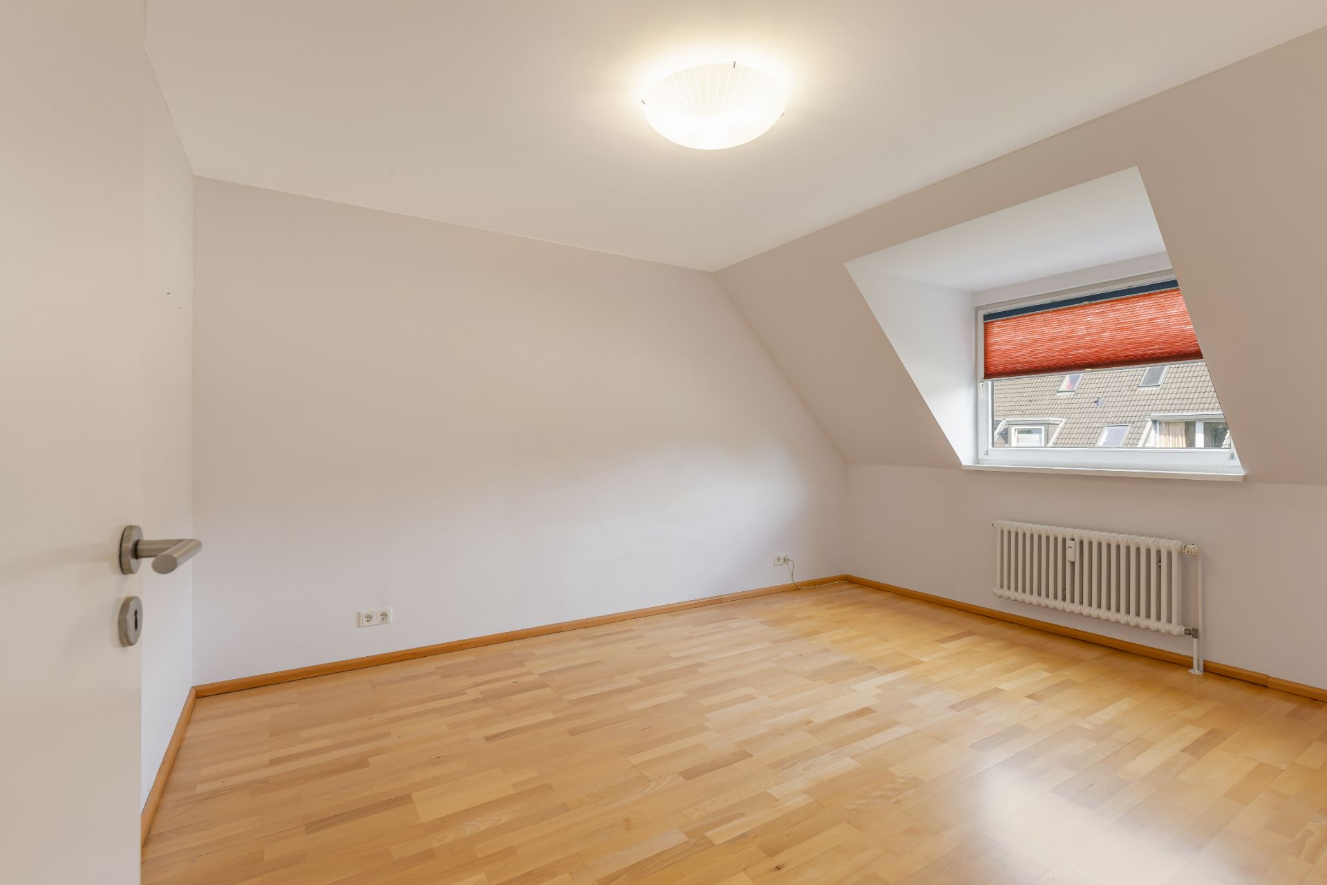 Leeres Zimmer mit Holzfußboden, Fenster, roter Jalousie und Heizkörper.