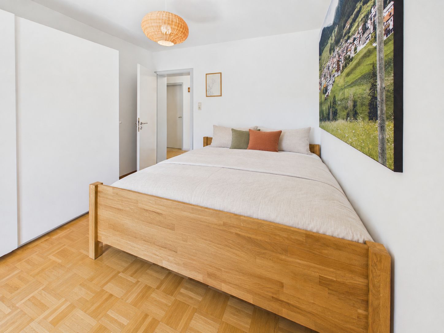 Helles Schlafzimmer mit Holzbett, weißem Schrank und Landschaftsbild an der Wand.