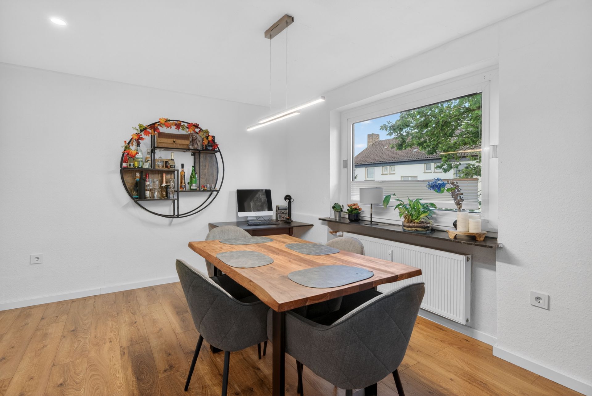 Essbereich mit Holztisch, vier Stühlen, großem Fenster, Regal und Zimmerpflanzen.
