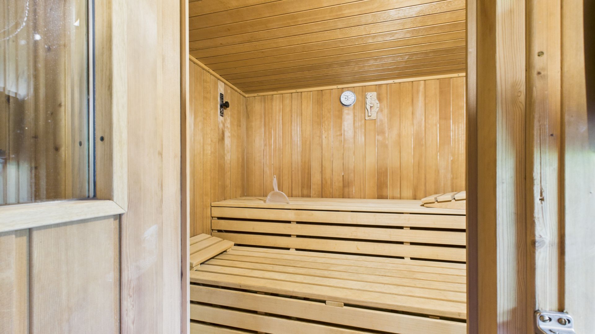 Helle Holzsauna mit zwei Bänken, Thermometer und Saunakelle an der Wand.