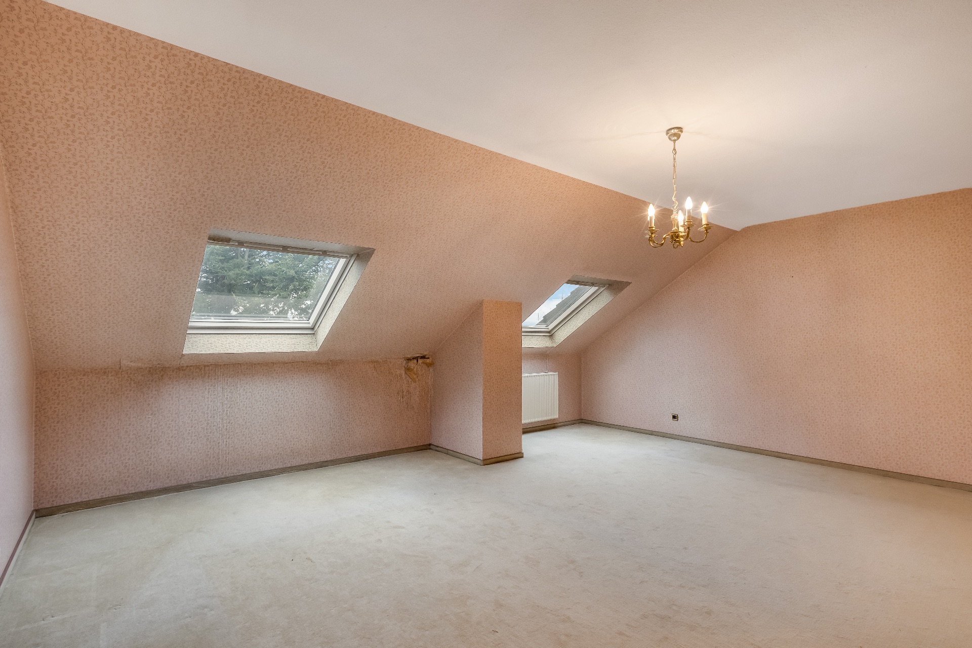 Leerer Raum mit Dachschräge, zwei Dachfenstern und Kronleuchter.